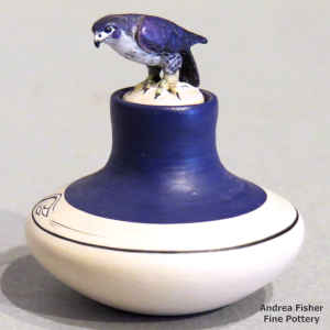 A miniature polychrome jar with a band of geometric design and a raptor sitting on the lid
