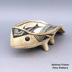 A black-on-white dish in the shape of a fish with four legs, a down-sloping tail and decorated on the outside with a fine line and geometric design and a fish, fine line and geometric design on the inside