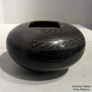 A cut square opening on a black on black jar with bands of geometric design