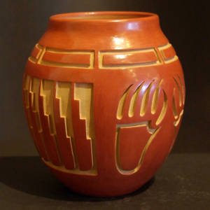 Bear paw, feather and geometric designs carved into a red jar