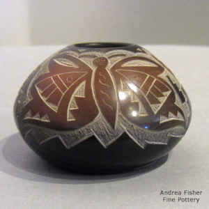 A sgraffito hummingbird, butterfly and geometric design on a miniature black seed pot with sienna spots