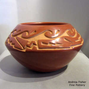 An avanyu and geometric design carved into a red jar