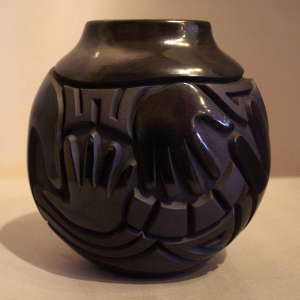 Hands and geometric design carved into a polished black jar