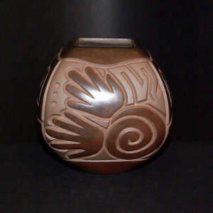 Hand, spiral and geometric design carved into a brown on brown jar