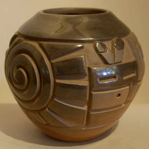 Spiral, katsina faces and geometric design carved into a black jar