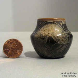 A sgraffito eagle, feather and geometric design on a black jar with a sienna rim