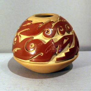 Double avanyu design carved into a red and tan jar
