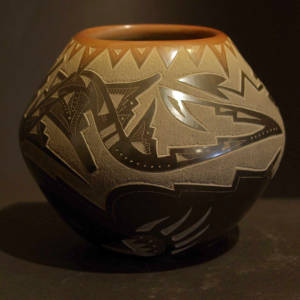 Sgraffito avanyu and bear paw designs on a black jar with a sienna rim