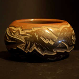 Sgraffito avanyu and bear claw designs decorate a black bowl with a sienna rim