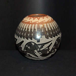 Sgraffito avanyu, feather, bear paw and geometric design on a black jar with sienna spots and a sienna rim