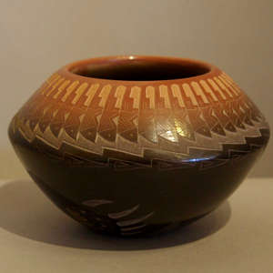 Sgraffito feather and bear paw design on a black pot with a sienna rim
