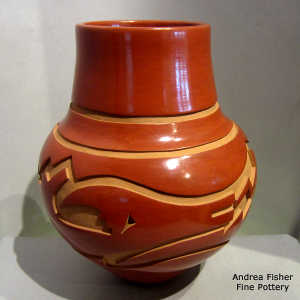An avanyu and geometric design carved into a red jar