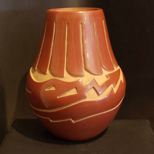 Feathers and an avanyu design carved into a red jar