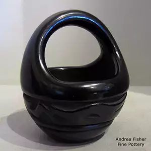 An avanyu design carved around the body of a polished black basket