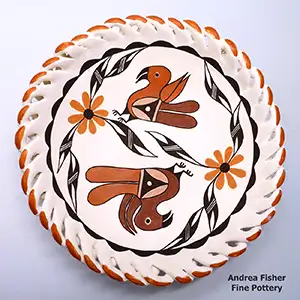 A polychrome plate with a braided rim around the dual parrot, branch, flower and geometric design on the face