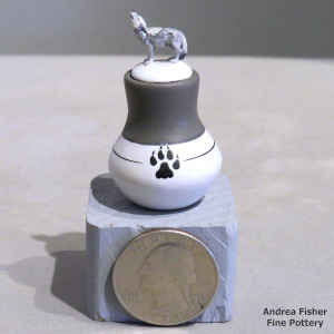 A miniature polychrome jar with a wolf paw print on the jar and a howling wolf on the lid