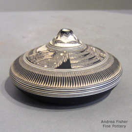 A black-on-white seed pot with a sgraffito wolf, feather and geometric design