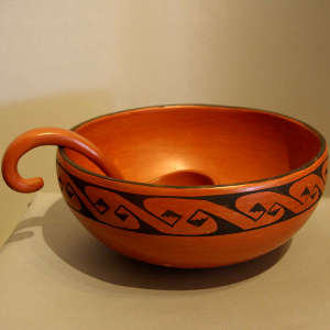 A band of black geometric design on a red bowl with a red ladle