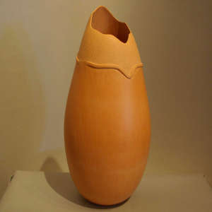 A raised ring and textured upper surface on a tan cylinder with an organic opening