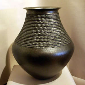 A wide corrugated band runs around the neck of this black micaceous jar with a rolled lip