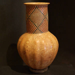 A band of checkerboard and geometric designs decorates the tall neck of this marbleized clay jar