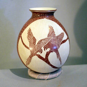 Sgraffito parrots, tree branch and geometric designs on a polished red jar