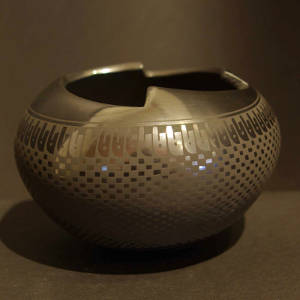 Checkerboard and other geometric designs decorate a black on black jar with a geometric cut opening