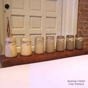 The same sgraffito and painted geometric design on a set of seven cylinders, each with a slightly darker body than the last and four knobs for handles around each shoulder