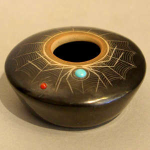 Sgraffito spider design and inlaid stones on a black jar with a sienna rim