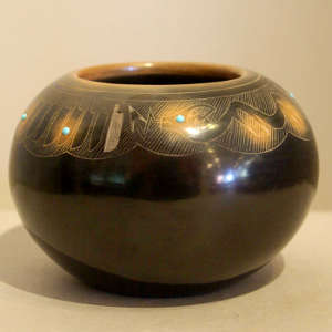 Sgraffito feather and avanyu design on a black jar with sienna spots and inlaid stones