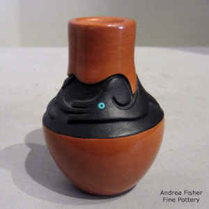 Black band carved with an avanyu design with an inlaid heishe bead eye on a red jar