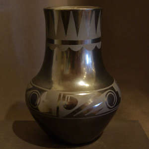 Bands of geometric designs around the rim and shoulder of a black on black tall neck vase