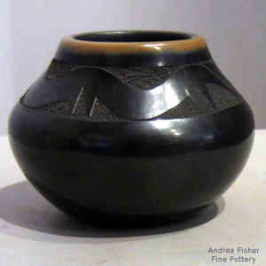 A sgraffito avanyu design on a black jar with a sienna rim