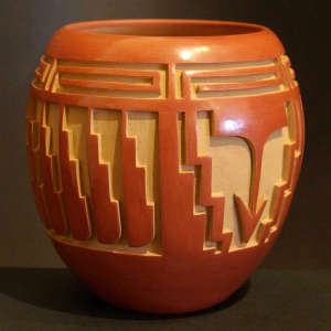 Feather, arrow and geometric design carved into a polished red jar