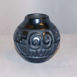 Spiral, sun face and geometric design carved into a black on black jar