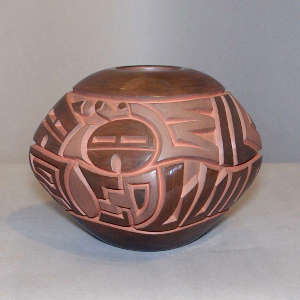 Sun face and geometric design carved into a squarish polished and matte brown jar
