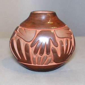 Spiral, hand and geometric design carved into a brown oblong jar