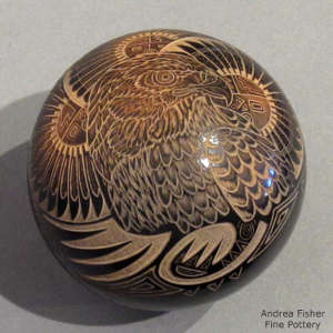 Sienna spot with sgraffito feather, sun face, hawk and geometric design on a black seed pot