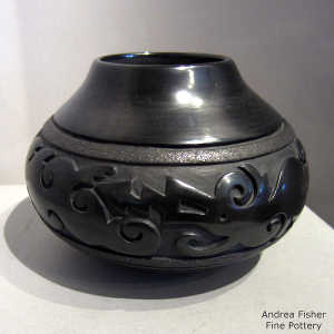 An avanyu design carved into a black jar with black micaeous bands
