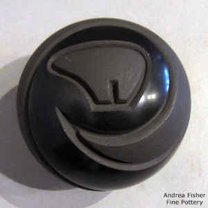 A spiral and bear design carved into a black ob black seed pot