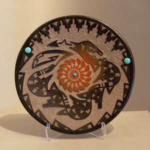 Sgraffito avanyu and geometric design on a black plate with a sienna spot in the center and inlaid stones