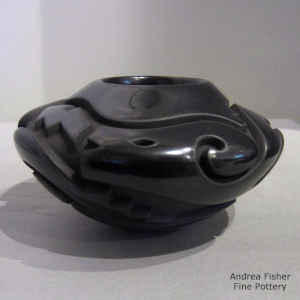 An avanyu, kiva step and geometric design carved into a glossy black bowl with a sgraffito flower design
