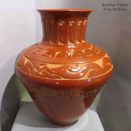 An avanyu, feather and geometric design carved into a red jar with a raised neck and flared rim