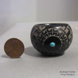 A sgraffito geometric design with an inlaid stone on a miniature black bowl