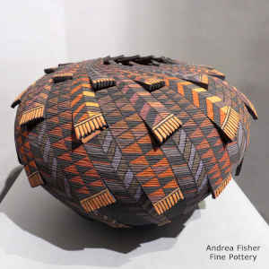 A tiny coil polychrome jar with cutouts and a painted geometric design